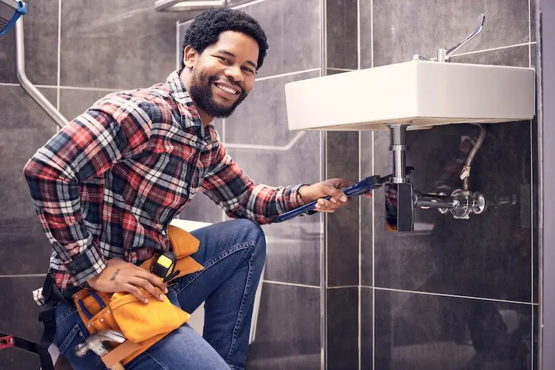 An emergency plumber bulimba sitting happy next to a sink he just fixed