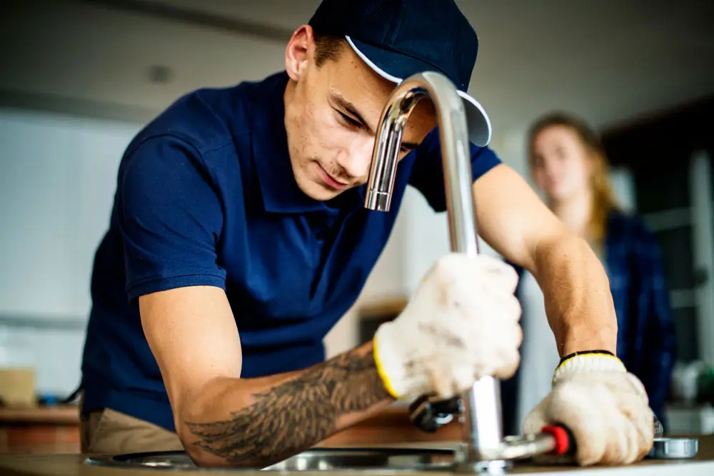 plumber in blue hard at work fixing and emergency plumbing problem