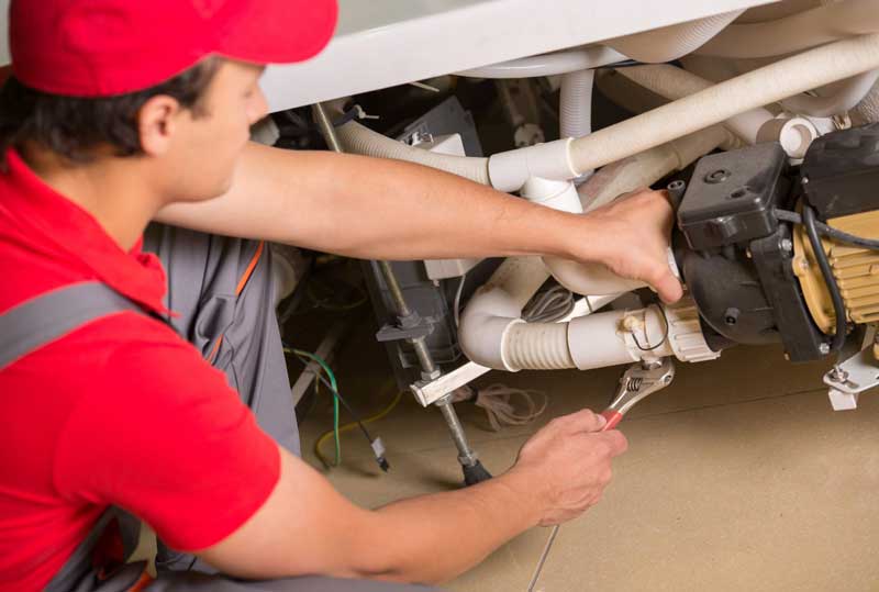Licenced plumber fixing plumbing pipes and pump under bathtub with wrench