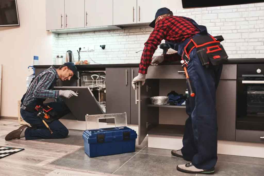 Two plumbers fixing a dishwasher, an example of what plumbers do in appliance maintenance