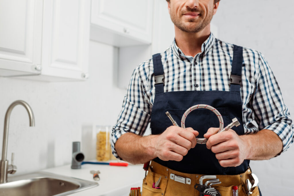Professional plumber in a checkered shirt holding a flexible connector, a key tool for ensuring drains are inspected regularly and maintained.
