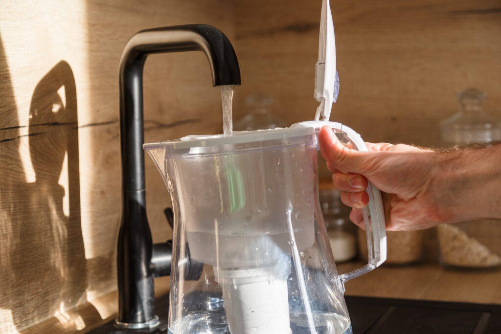 A person filling a pitcher from the tap, prompting concerns about water clarity: "Why is my tap water cloudy?"