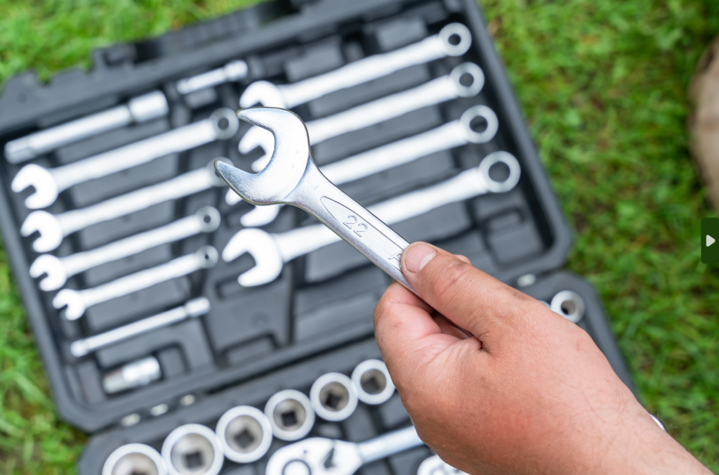 Person holding a wrench from a toolbox filled with tools, essential for learning how to fix leaking taps efficiently.
