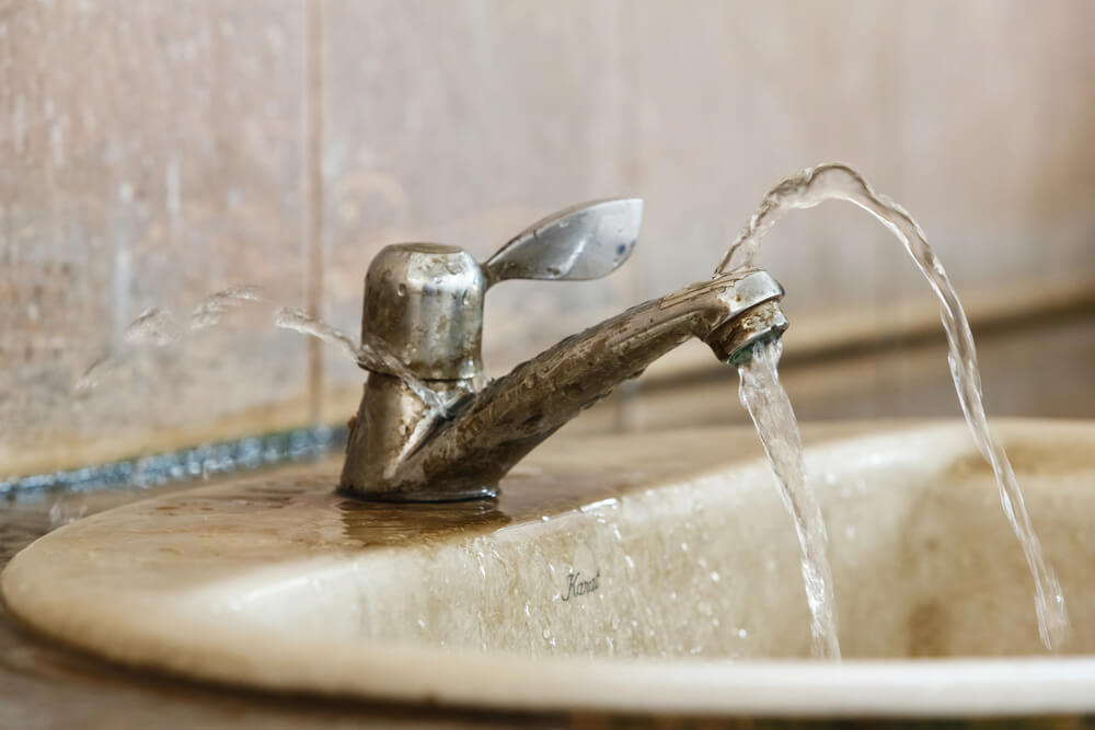 A damaged kitchen faucet with water spraying uncontrollably from the sides, exemplifying what is considered a plumbing emergency that requires immediate repair to prevent wastage and damage.