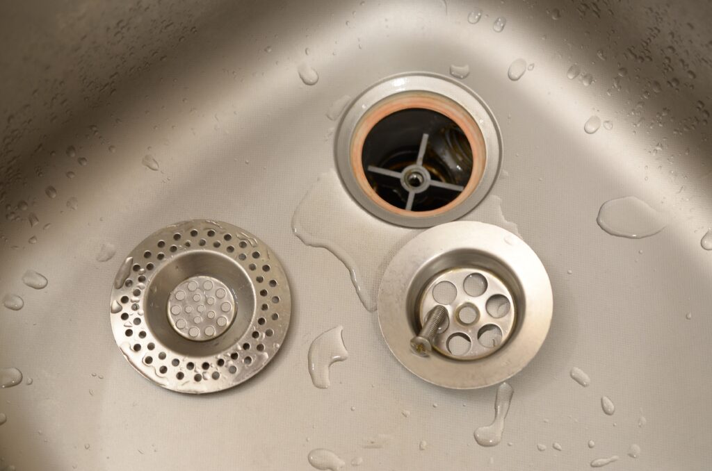 Silvery kitchen sink with a disassembled protective filter during the repair process, raising the question of how much is emergency plumbing, including emergency plumber costs and call out fees in Brisbane.