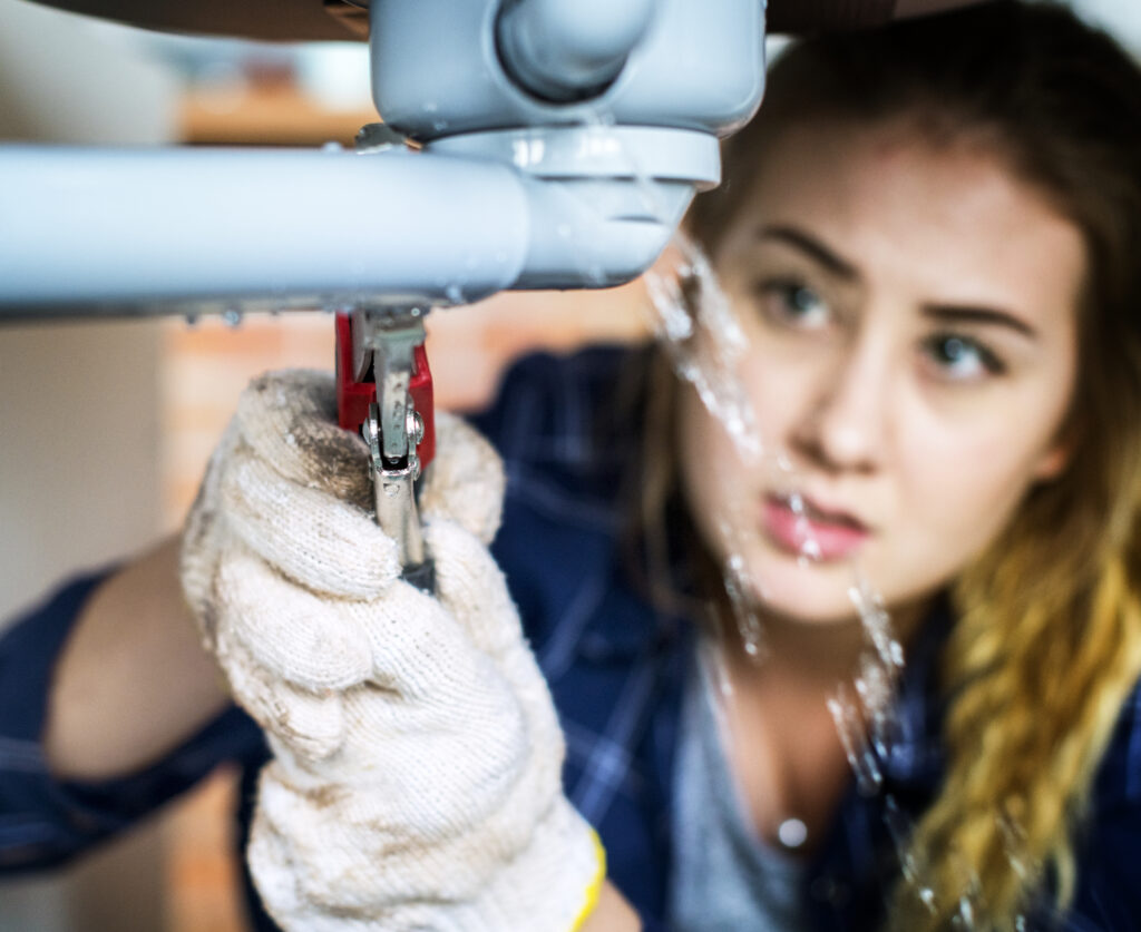 A woman fixing her own toilet sink, contemplating how much is emergency plumbing, and considering the cost of emergency plumbing services in Brisbane, including plumber call out fees.