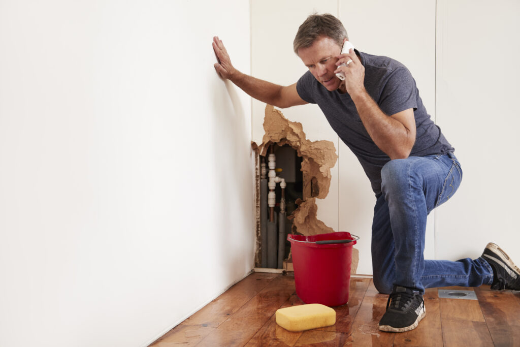 A man kneels on the floor, looking concerned as he makes a phone call to a loval emergency plumber.
