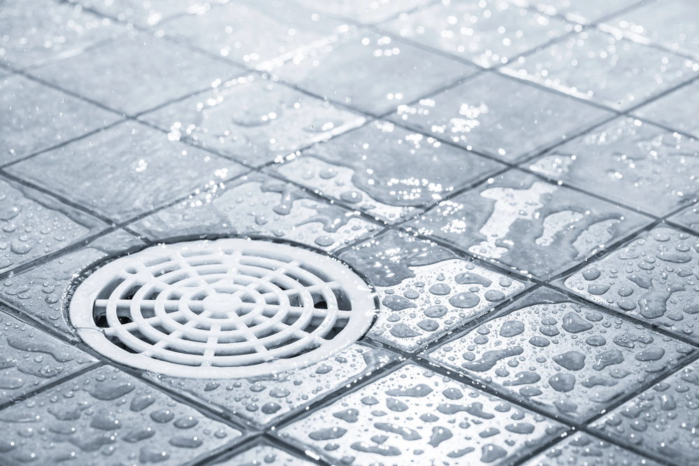 A close-up of a wet tiled floor with a clean drain, emphasizing the importance of regular cleaning to help prevent blocked drains