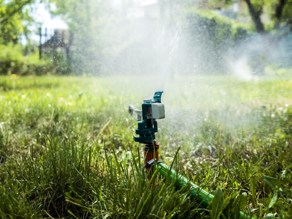 Water splashing on a green lawn from a garden sprinkler during summer, symbolising outdoor water conservation through Sustainable Plumbing Solutions.